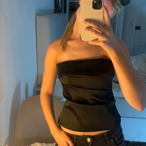 Svart satin tubtopp från Zara - Säljer en svart bandeutopp från Zara i satinaktigt material. Använd 1 gång endast så i väldigt bra skick. Perfekt som festtopp! 