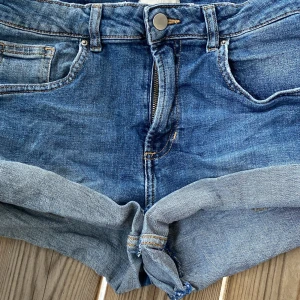 Blå lågmidjade jeansshorts med upprullad kant - Snygga blå jeansshorts med upprullad kant och lågmidjade. Använda ganska mycket och trådar hänger från byxorna men jag vek upp dem och storleken passar XS S och M. Lågmidjade shorts från H&M!