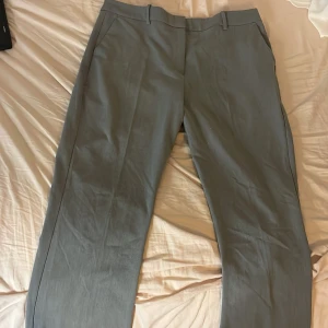 Grå kostymbyxor med raka ben från bik bok - Snygga grå kostymbyxor med klassisk rak passform och hällor för bälte. Byxorna har diskreta sidfickor och är tillverkade i ett slätt tyg som ger en clean look. Perfekta för dig som gillar stilrena och tidlösa plagg. Ny pris 499kr