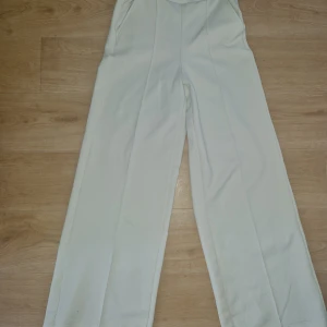 Vita wide byxor från Gina Tricot XS - Säljer ett par vita byxor från Gina Tricot i storlek XS. Byxorna har breda ben, hög midja och är tillverkade i ett mjukt, strukturerat tyg. De har fickor i sidorna och en clean look som passar till många olika stilar.