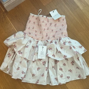 Blommig volangkjol från By Malina - Supersöt kort kjol från By Malina med volanger och smockad midja. Lapparna är kvar, kjolen är HELT oanvänd!!