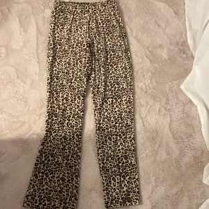 Leopardmönstrade byxor Gina Tricot XS - Leopardmönstrade byxor från Gina Tricot i stretchigt material. Byxorna har normal passform, rak modell och resår i midjan. Färgerna går i beige, brunt och svart. Perfekta för dig som vill sticka ut med ett djurmönster.