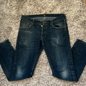 Mörk blå lee jeans - Snygga mörkblå Lee jeans med klassisk design. De har en knappgylf och femficksmodell. Perfekta för en stilren look.