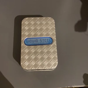 Liquid Steel herrparfym 100ml - Hej ganska random parfym men luktar fett gott Snygg herrparfym i robust industridesign. Flaskan är rektangulär med blått glas och har en metallisk platta med rutmönster och texten 'Liquid Steel'. Kommer i matchande metallask. Doften är eau de toilette och rymmer 100 ml.