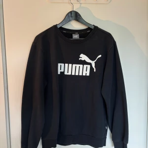 Svart sweatshirt från Puma i bomull - Svart sweatshirt från Puma med stor vit logga framtill. Klassisk rund halsringning och långa ärmar. Tillverkad i mjuk bomullsmix som är skön att ha på sig. Perfekt för en avslappnad och sportig stil.
