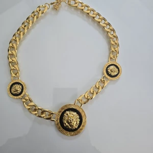  Guldfärgad halsband med lejonmotiv - Statement halsband i chunky guldfärgad metall med tre runda medaljonger, var och en prydd med ett detaljerat lejonhuvud i guld mot svart bakgrund. Kedjan är kraftig och har klassisk karbinlås. Perfekt för dig som vill sticka ut med en lyxig vibe.