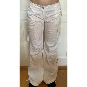 Vita cargopants med fina detaljer - Säljer ett par vita cargopants med flera fickor och coola detaljer som snörning vid benslut och midja. Innerbensmått: 81cm. Midja rakt över: 39,5cm. Modellen på bilden är 157cm och står lite på tå.