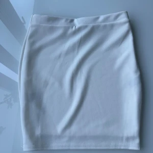 Vit kjol - Enkel och stilren vit kortkjol i stretchigt material. Kjolen har en tight passform och är helt utan mönster eller detaljer, vilket gör den lätt att matcha med olika toppar. Perfekt för dig som gillar en clean och minimalistisk look