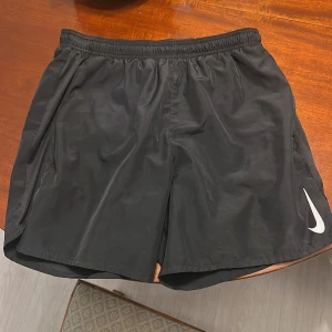 Svarta Nike Dri-FIT träningsshorts - Svarta träningsshorts från Nike med Dri-FIT-teknologi. De har elastisk midja, sidofickor och en diskret Nike-logga på ena benet. Lätta och luftiga, perfekta för sport eller gym. Klassisk loose passform och tillverkade i syntetmaterial. Hör av vid frågor!🙌🏽 Pris går alltid att diskuteras!