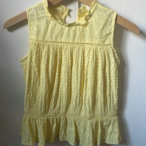 Gul ärmlös blus med volang - Söt ljusgul blus med broderade detaljer upptill och volangkant nertill. Superfin!! Storlek 11/12 men passar xxs-xs perfekt!🥰