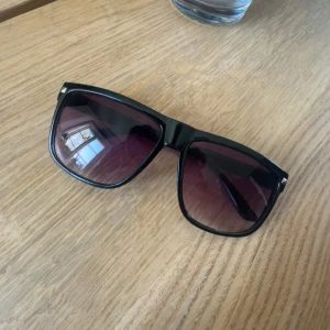 Svarta solglasögon med lila tonade glas - Stilrena solglasögon med svart, fyrkantig båge och lila tonade glas. Snygg och modern design som ger en cool vibe. Perfekta för att lyfta din look under soliga dagar.