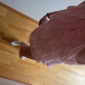 Rosa volangklänning med omlottkänsla - Supersöt kort rosa klänning med flera lager volanger och omlottkänsla. Klänningen är ärmlös och har en lätt och luftig känsla, perfekt för varma dagar. 