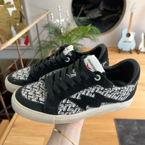 Zadig & Voltaire svartvita sneakers - Snygga sneakers från Zadig & Voltaire med svartvitt grafiskt mönster och svarta mockadetaljer. Skorna har vita sulor, svarta snören och en vit plös med röd logga. Perfekta för dig som gillar streetstyle och vill sticka ut.