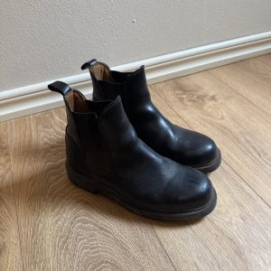 Svarta boots i skinn - Klassiska svarta kjängor med elastiska paneler på sidorna och dragflikar både fram och bak. Grov sula för extra grepp och rund tå. Har används i stallet.