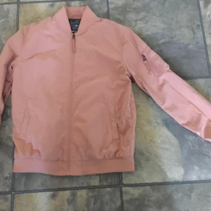 Ljusrosa bomberjacka Jack & Jones - Snygg ljusrosa bomberjacka från Jack & Jones Originals i storlek medium. Jackan har klassisk bombermodell med dragkedja framtill, fickor på sidorna och en extra ficka med dragkedja på ärmen. Tillverkad i polyester och perfekt för dig som vill sticka ut med en fräsch färg..