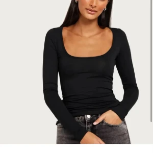 Svart långärmad topp med fyrkantig ringning - Snygg svart långärmad topp med djup fyrkantig ringning och tight passform. Perfekt att styla med jeans eller kjol för en clean look. Tunn och stretchig, vilket gör den superbekväm och enkel att bära hela dagen.