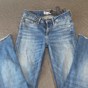 Blå bootcut från Zara - Snygga blå jeans från Zara med klassisk femficksmodell. Jeansen har ljus tvätt och råa, avklippta benslut för en trendig look. Perfekta till sneakers eller boots och passar till många olika stilar.