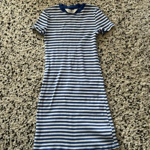 Randig blåvit kortklänning H&M - Superfin ribbad kortklänning från H&M i blått och vitt med klassiskt randigt mönster. Klänningen har korta ärmar, rund halsringning och en slim passform som sitter snyggt. Perfekt för en chill sommardag eller när du vill vara casual men ändå stilren.