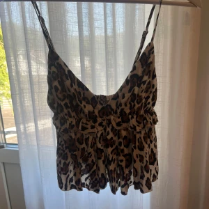 Leopardmönstrad tipp - Supersöt blus med leopardmönster och tunna justerbara axelband. Toppen har volangdetaljer längs bysten och en luftig, flowy passform. Perfekt för dig som vill sticka ut med en cool vibe till sommaren eller fest! Helt ny med prislapp!! 