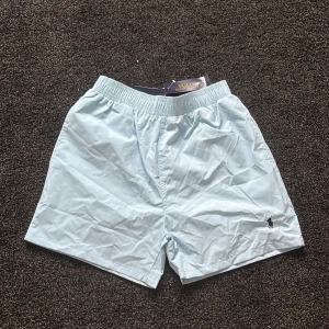 Ljusblå shorts från Polo Ralph Lauren - Snygga ljusblå shorts från Polo Ralph Lauren med klassisk broderad logga på benet. De har elastisk midja och en bakficka med lock. Perfekta för sommardagar och chill vibes. Materialet känns lätt och luftigt, vilket gör dem riktigt sköna att bära.