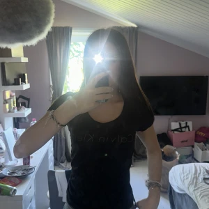 Svart Calvin Klein t-shirt - Svart t-shirt från Calvin Klein med klassisk logga framtill. Modellen är figurnära med korta ärmar och rund halsringning. Perfekt basic-plagg med stilren design, passar till jeans eller kjol. Materialet känns mjukt och skönt mot huden.