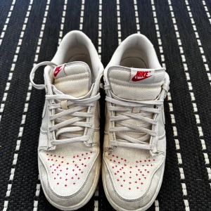 Nike Dunk Low Sashiko vit/röd - Nike Dunk Low Sashiko i ljus orewod brown med vit canvas och röda broderade detaljer. Klassisk låg sneaker med snörning, röd Nike-logga på plös och häl samt unika röda sömmar på tån. Perfekt för dig som gillar stilrena men ändå unika sneakers. Köpta 2 år sedan, knappt använda 