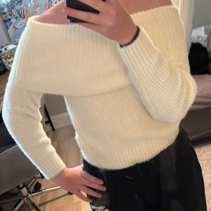 Offshoulder stickad tröja H&M Divided - Superfin offshoulder stickad tröja från H&M Divided i krämvit färg. Tröjan har ribbad struktur, lång ärm och bred krage som sitter snyggt över axlarna. Perfekt att styla med jeans eller kjol för en trendig look.