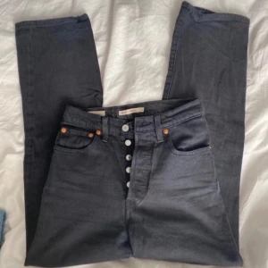 Levi's Ribcage Straight svarta jeans W24 - Snygga svarta Levi's Ribcage Straight jeans med hög midja och raka ben. Klassisk femficksmodell med knäppning framtill och detaljer i silver. Jeansen är i bomull och har en stilren look som passar till allt.