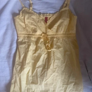 Gult linne från edc! - Gult babydoll linne från edc med smala axelband, v-ringning och volangkant upptill. Klänningen har knytband i midjan och är i superlätt material. Gullig broderad detalj på bröstet💕står som strl L men passar mer som M. Obs! Gulare i verkligheten