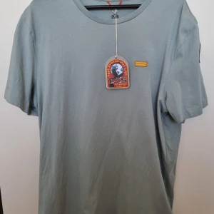 Turkos iconic t-shirt från Parajumpers - Snygg ljusblå t-shirt från Parajumpers med klassisk rund hals och korta ärmar. T-shirten har en liten gul detalj på bröstet och ett broderat PJS-märke på ärmen. Tillverkad i mjuk bomull för en skön känsla.