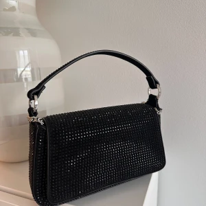 Svart glittrig axelväska med kedja - Snygg svart axelväska med glittriga detaljer och silverfärgad kedja. Köpt på Mango använd en gång. Nyskick - Mycket bra skick