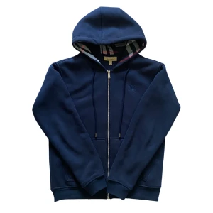 Marinblå hoodie från Burberry - Snygg marinblå hoodie från Burberry med dragkedja och klassiskt rutigt foder i huvan. Tillverkad i 100% bomull för en skön känsla. Broderad logga på bröstet och praktiska fickor framtill. Perfekt för dig som gillar stilrena och exklusiva plagg.