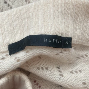 Offshoulder stickad tröja från Kaffe - Supersöt offshoulder stickad tröja i ljusbeige från Kaffe. Tröjan har långa ärmar, bruna hjärtan med paljetter och snörningsdetalj upptill. Mjuk och mysig, perfekt för höst och vinter. Unik design som sticker ut! 