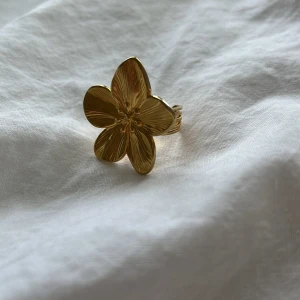Guldig blomformad ring - Superfin ring i guld med en stor blomformad design. Ringen har detaljerade blad och en glansig finish som verkligen sticker ut. Perfekt accessoar för dig som vill ha något unikt och trendigt.