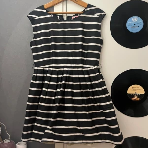 Randig kortklänning från Pernilla Wahlgren  - Snygg svart och vit randig kortklänning från Pernilla Wahlgren . Klänningen är ärmlös med rund halsringning, markerad midja och utställd kjol. Dragkedja i guld baktill ger en cool detalj. Perfekt för dig som gillar klassisk men trendig stil.