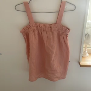 Rosa linnetopp från WAI WAI - Supersöt rosa linnetopp från WAI WAI med breda axelband och rynkad kant upptill. Luftig och skön modell i linne, perfekt för varma dagar. Enkel men trendig design som är lätt att matcha med jeans eller kjol. Strl 170. Aldrig använd. 