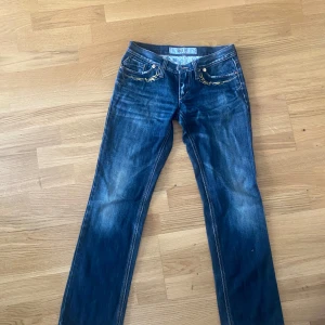 Blå jeans från Take Two med brodyr - Snygga blå jeans från Take Two med guldiga broderier på fickorna fram och bak. Klassisk femficksmodell med raka ben och låg midja. Jeansen har  detaljer som ger en cool vintagekänsla. Storleken känns som S eller XS, är ungefär 159 och då är längden som vilka jeans som helst 
