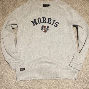 Grå stickad tröja från Morris Gents - Snygg grå stickad tröja från Morris med broderad logga och emblem på bröstet. Tröjan har rund hals, ribbade muddar och lång ärm. Perfekt för dig som gillar klassisk och stilren look. Den är i mycket fint skick. Va inte rädd för att ställe frågor🙌🤝🤝
