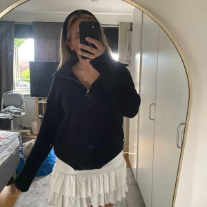 Svart stickad half zip från Cherry Koko - Svart stickad tröja från Cherry Koko med halv dragkedja och hög krage. Tröjan har lång ärm och en loose fit som ger en chill vibe. Perfekt att slänga på sig när det är kallt ute. Enkel och stilren design som funkar till det mesta.