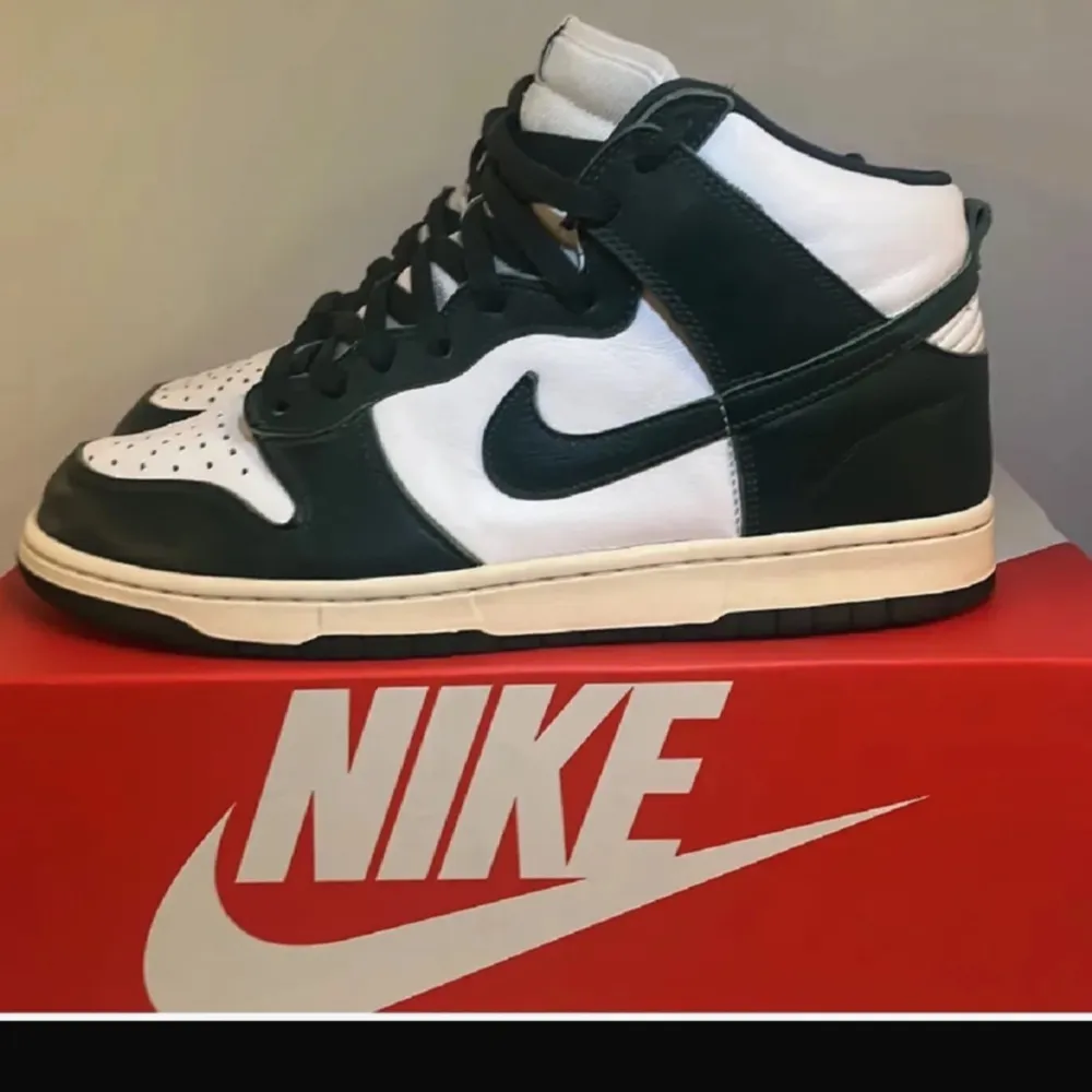 Snygga Nike Dunk High i färgen Spartan Green. Skorna har en klassisk design med vit och grön färgkombination. Perfekta för dig som älskar stilrena sneakers med en sportig touch. De har snörning och en hög siluett som ger extra stöd.. Kengät.