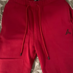 Röda mjukisbyxor från Jordan - Snygga röda mjukisbyxor från Jordan med elastisk midja och dragsko. Byxorna har en broderad logga på sidan och en bakficka. Perfekta för en avslappnad stil.