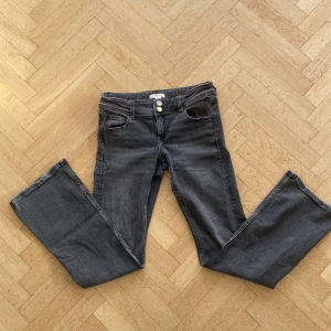 Grå jeansbyxor från Gina Tricot - Snygga mörkgrå jeansbyxor från Gina Tricot med två knappar i midjan och klassisk femficksdesign. Byxorna är utsvängda där ner/ Bootcut. De är tillverkade i ett bekvämt denimtyg som ger en skön känsla hela dagen. Storlek 158 och ungefär 1 år gammal. 