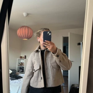 Beige jacka med knappar - Säljer en stilren beige jacka med stora knappar framtill. Jackan har en klassisk krage och två stora fickor på bröstet. Perfekt för höst och vår! Den är kortare i modellen och knappt använd