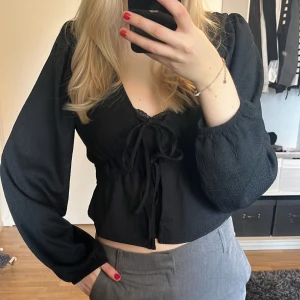 Svart blus med knytning - Säljer en stilren svart blus med knytning framtill. Blusen har långa ärmar och en lätt croppad passform. Perfekt att både klä upp och klä ner❣️ använd fåtal gånger