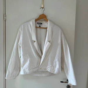 Vit kavaj från Idem Paris - Säljer en stilren vit kavaj från Idem Paris. Kavajen har en klassisk design med knappar framtill och långa ärmar. Perfekt för en elegant look. 