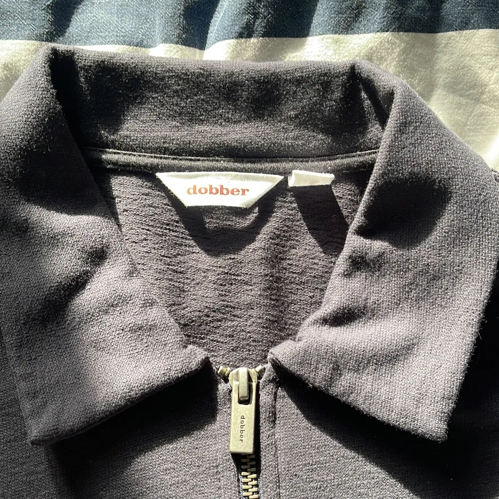 Snygg svart långärmad pikétröja från Dobber med dragkedja vid halsen. Perfekt för en stilren och avslappnad look. Tröjan har en klassisk krage och är tillverkad i ett bekvämt material.. Neuletakit & Villapaidat.