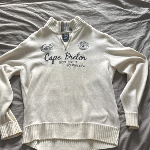 Vit tröja med Cape Breton-tryck från Lerros - Säljer en vit tröja från Lerros med Cape Breton Nova Scotia-tryck. Tröjan har en dragkedja vid halsen och ribbade muddar vid ärmslut och nederkant. Perfekt för en avslappnad stil. Obs skicket på bilderna noggrant.