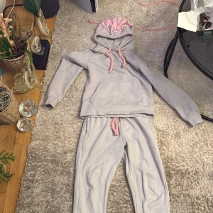 Grå hoodie med rosa detaljer - Säljer en grå hoodie med rosa snören och tryck. Hoodien har en stor ficka framtill och texten 'Forgive Me' broderad på ärmen. Perfekt för en avslappnad stil.