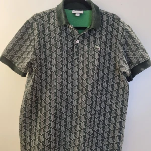 Grön mönstrad pikétröja från Lacoste - Grön pikétröja från Lacoste med knappar i kragen.