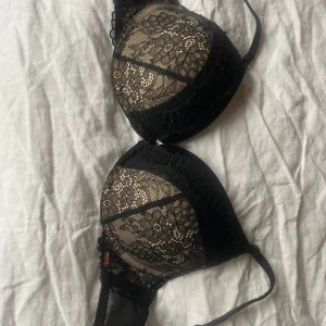 Svart spets-bh från Hunkemöller Noir - Elegant svart bh från Noir med vacker spetsdetalj. Den har justerbara axelband och en mjuk insida för extra komfort. Perfekt för att känna sig både bekväm och stilfull.
